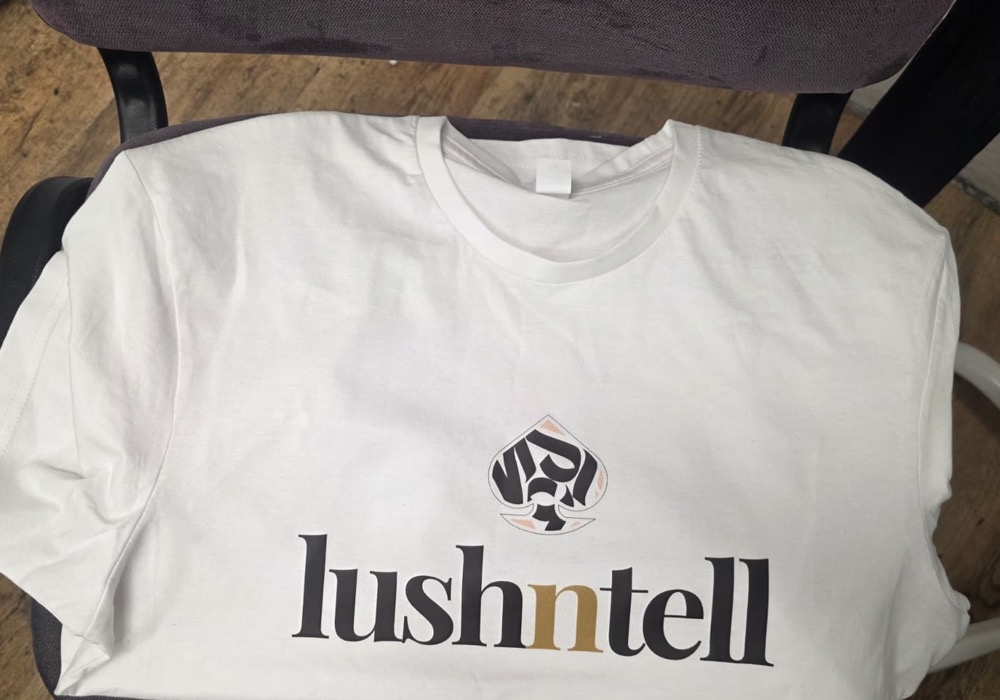 White t-shirt printed with a clothing brand logo in black and gold, photographed at the IT Wheel workshop in London